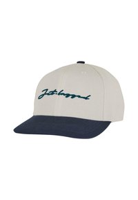 Gorra de béisbol con una corona de tela beige, visera azul oscura y texto cursivo bordado en color teal que dice "Jet-lagged" en el frente.