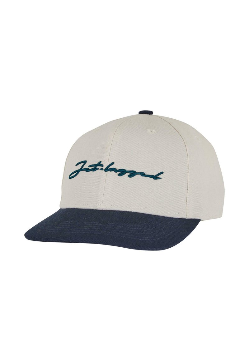 Gorra de béisbol con una corona de tela beige, visera azul oscura y texto cursivo bordado en color teal que dice "Jet-lagged" en el frente.