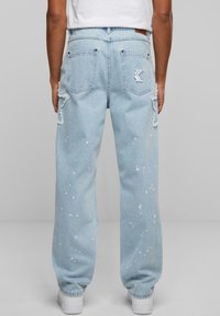 Light blue denim jeans with a loose fit, distressed detailing, paint splatters, and two back pockets featuring an embroidered logo.
