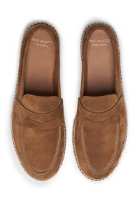 Mocasines de ante marrón en estilo mocasín, con un detalle de correa en la parte delantera, costuras blancas y una plantilla de cuero suave. Fabricados en España.