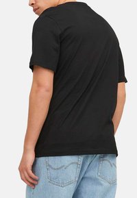Black cotton t-shirt with short sleeves and a round neckline, worn by a person. Paired with light blue denim jeans.