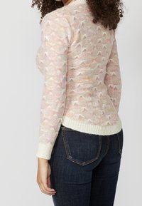 Suéter de punto con un diseño de bordes en colores pastel, con un dobladillo y puños acanalados de color crema claro. Se lleva con vaqueros de color azul oscuro.