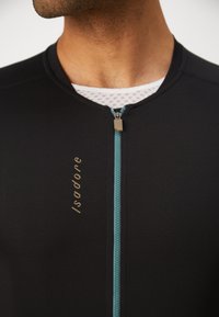 Svart cykeltröja med rund halsringning och en teal dragkedja. Har en guldtextlogotyp på framsidan. Snyggt, stretchbart tyg med en slät yta.