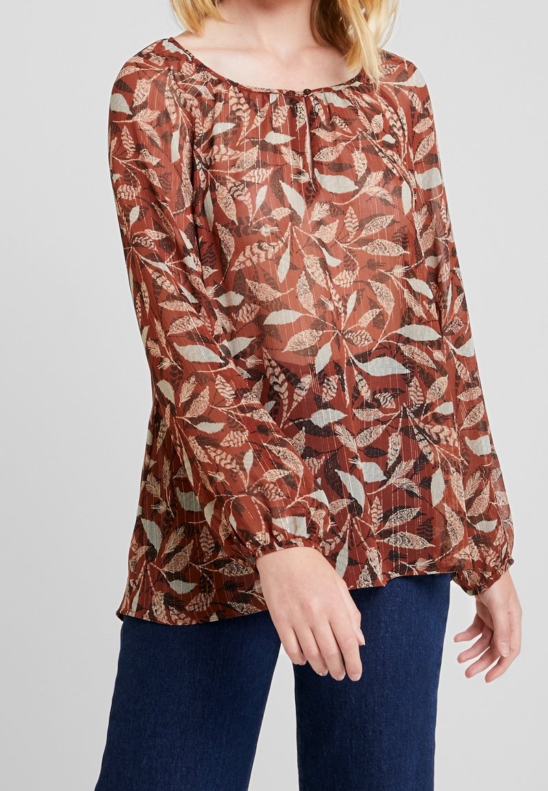 Blouse marron à motif de feuilles avec un col froncé et des manches longues légèrement bouffantes ; fabriquée en tissu léger et texturé.