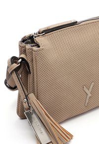Borsa a tracolla in pelle beige perforata con chiusura a zip, dettagli metallici e un accento in frangia con un'etichetta del marchio attaccata.