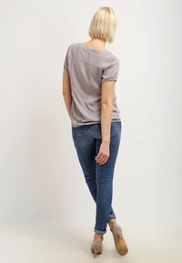 Grå polkaprikket bluse med korte ærmer, kombineret med mørkeblå skinny jeans og beige højhælede sko, set bagfra.