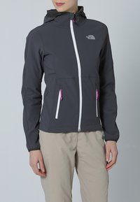 Dunkelgraue Softshell-Jacke mit tailliertem Design, weißem Reißverschluss und rosa Akzenten. Verfügt über eine Kapuze und zwei vordere Reißverschlusstaschen.