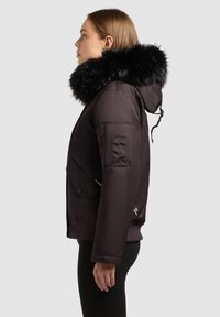 Schwarze Daunenjacke mit abnehmbarem, mit Pelz gefüttertem Kapuzen, mit Reißverschluss Taschen an den Seiten und gerippten Bündchen. Glatte Außenfläche mit glänzendem Finish.