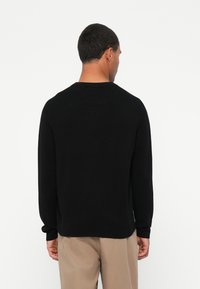 Suéter preto de mangas compridas com decote redondo, feito de um material suave, apresentando mangas com punho e um corte descontraído.