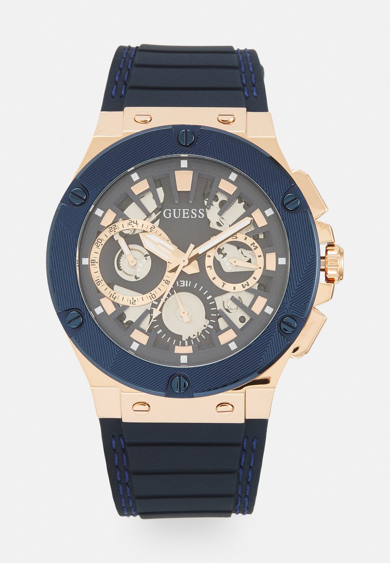 Chronograph-Uhr mit einem navyblauen Silikonarmband, Roségold-Akzenten und einem transparenten Zifferblatt, das mehrere Anzeigen und Stundenmarkierungen zeigt.