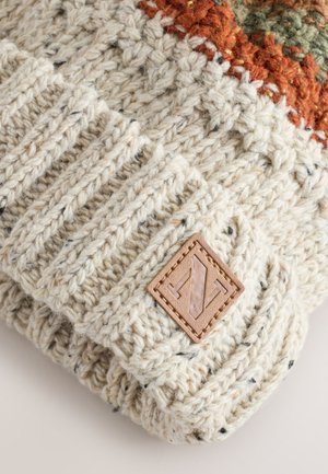 Heledad helesinisest kootud müts tekstuursete mustritega, millel on tumedad täpid ja pruun nahast logomärk.