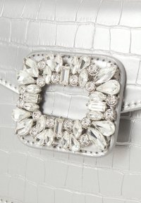 Srebrna torebka ze wzorem krokodyla, zdobiona klamrą wysadzaną kryształami o różnych kształtach łezki i okrągłych. Gładka tekstura i elegancki design.