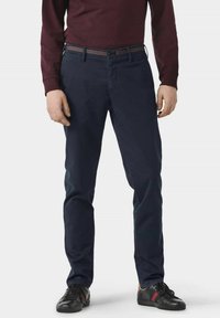 Marineblaue Baumwoll-Chinos mit leicht schmalerem Schnitt, kombiniert mit schwarzen Sneakers mit roten und grünen Akzenten sowie einem kastanienbraunen Langarmoberteil.