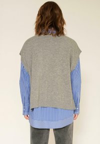 Pull en peluche gris surdimensionné à manches courtes superposé à une chemise à boutons rayée bleue et blanche. Tissu doux avec une coupe décontractée.