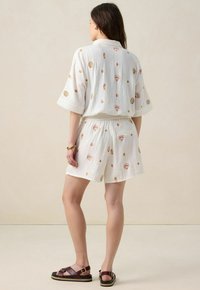 Ensemble en tissu texturé blanc comprenant une chemise à manches courtes et un short assorti, ornés de motifs de coquillages et de points dans des couleurs pastel.