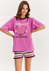 Růžové bavlněné tričko s krátkým rukávem, zdobené barevným grafickým potiskem. Spárováno s multibarevnými pruhovanými háčkovanými šortkami.