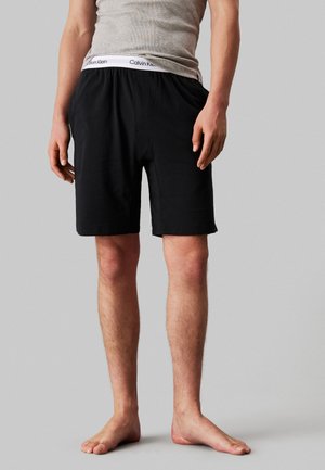 Pantaloni corto neri in cotone con vita elastica, dotati di etichetta bianca con marchio, texture liscia e taglio a lunghezza ginocchio.