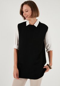 Musthave mustrikk varrukateta sviiter valge kraega särgi peal, ümmarguse kaeluste ja soonikuga alläär. Sile tekstuur ja lõdvestatud lõige.