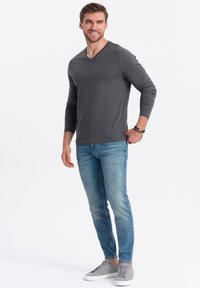 Graues langärmeliges V-Ausschnitt-Shirt kombiniert mit hellblauen Slim-Fit-Jeans und grauen Sneakern, mit einem schlichten Design ohne Muster oder Logos.