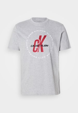 Gray cotton t-shirt featuring round neckline, short sleeves, and a central graphic with "Calvin Klein" and "CK" in red and black.