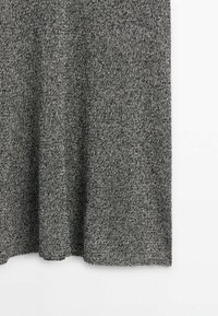 Tissu tricoté gris avec une texture tachetée et un ourlet droit sur fond blanc.
