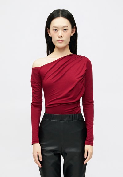 Top borgogna off-the-shoulder con maniche lunghe, caratterizzato da un design drappeggiato. Abbinato a pantaloni neri in finta pelle lucida a vita alta.