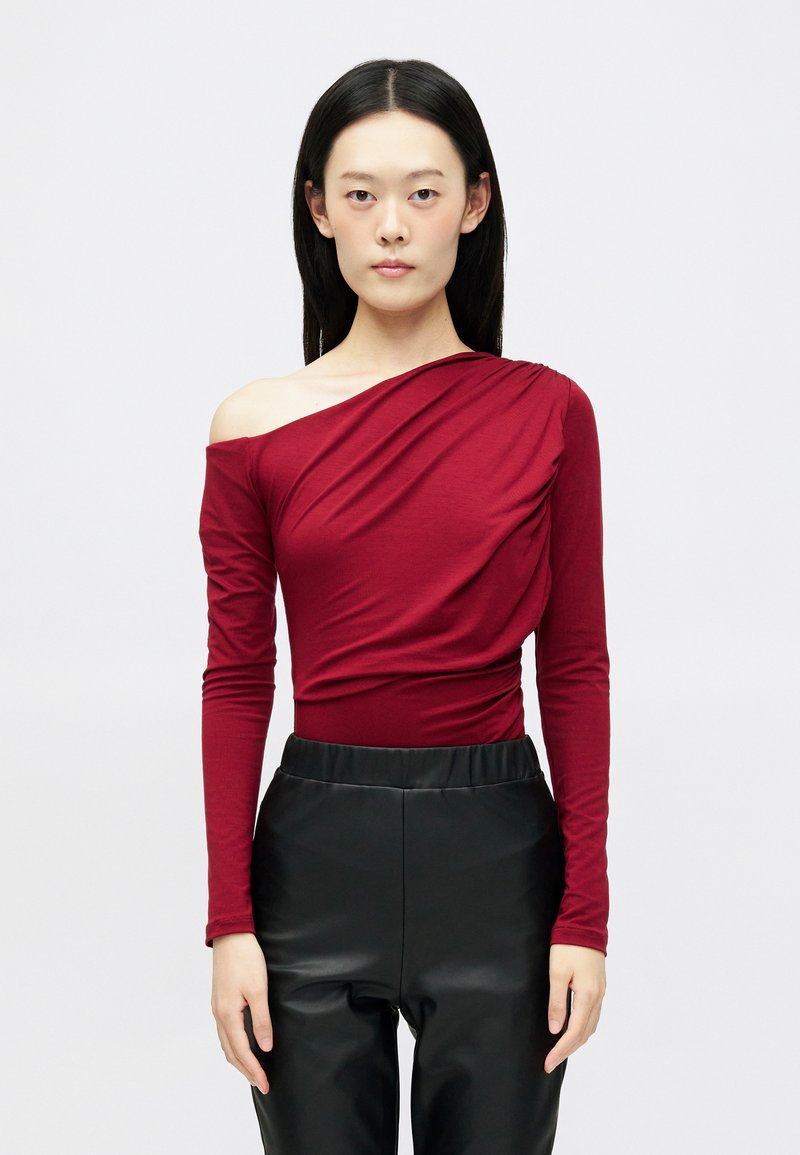 Top bordô de ombros à mostra com mangas longas, apresentando um design drapeado. Combinado com calças pretas de cintura alta em imitação de couro brilhante.
