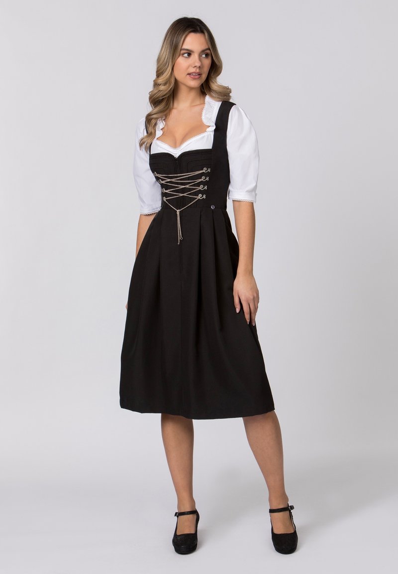 Schwarzes Dirndl mit tailliertem Oberteil, weißer Bluse, Schnürdetails an der Vorderseite und gefälteltem Rock, kombiniert mit schwarzen Schuhen.