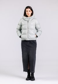 Lys grå pufferjakke med høj krave, lynlåslukning og quiltet design, parret med en sort denimnederdel og sorte snørebåndsstøvler.