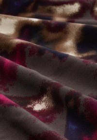 Musterstoff in einer Mischung aus tiefem Burgunderrot, Braun und dunklen Blautönen mit einer glatten Textur und sanftem Glanz.