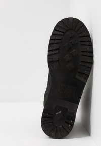 Zwarte rubberen zool met diepe profielranden, voorzien van een gestructureerd oppervlak en een logo-afdruk. Ronde neus en stevige constructie.