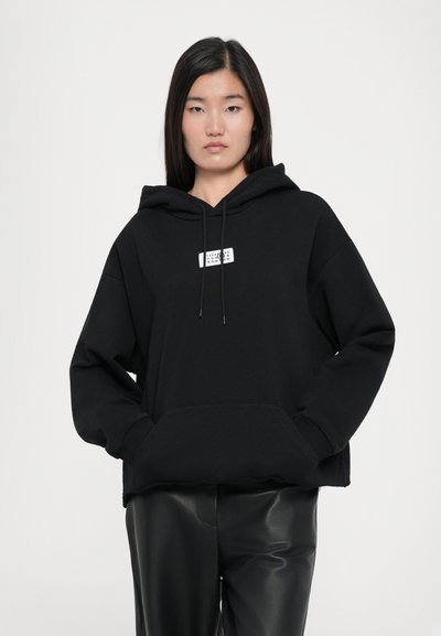 Svart cropped hoodie tillverkad av mjukt tyg, med en vit logotyp på bröstet, justerbar dragsnodd i huvan och framficka.