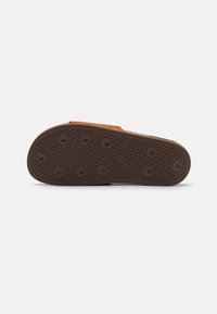 Suola di scarpa in gomma marrone con un motivo testurizzato, presenta impugnature circolari e una forma piatta. Non sono visibili dettagli o accenti distintivi.