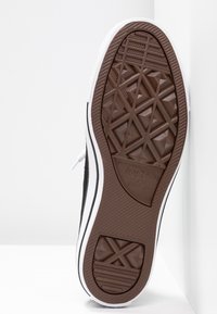 Semelle de sneaker noire avec un motif en caoutchouc brun texturé, dotée de bandes blanches sur les côtés et d'un logo. Conçue pour l'adhérence et la durabilité.