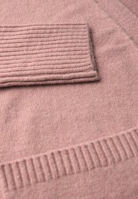 Pull en tricot rose avec un détail de poche côtelée. Texture douce, présentant un corps lisse et un ourlet côtelé, mettant en valeur une légère variation de couleur.