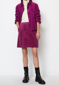 Ensemble de chemise en velours côtelé magenta avec jupe assortie. La chemise a une poche et des boutons. Associée à des bottines noires et un pull col roulé blanc.