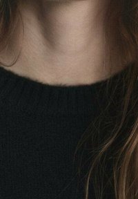 Maglione nero lavorato a maglia con scollo rotondo, con una texture a coste e sottili ciocche di capelli castano chiaro visibili sullo sfondo.