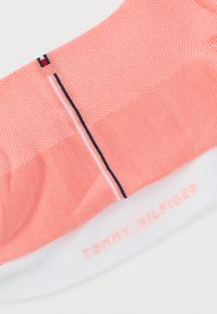 Λεπτομέρεια ροζ κάλτσας με υφή, με ριγέ σε ναυτικό μπλε, λευκό και κόκκινο και την επωνυμία "Tommy Hilfiger" σε λευκή μανσέτα.