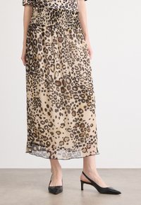 Jupe midi imprimée léopard en tissu transparent avec une taille smockée, offrant une forme évasée et un détail d'ourlet subtil, associée à des escarpins noirs.