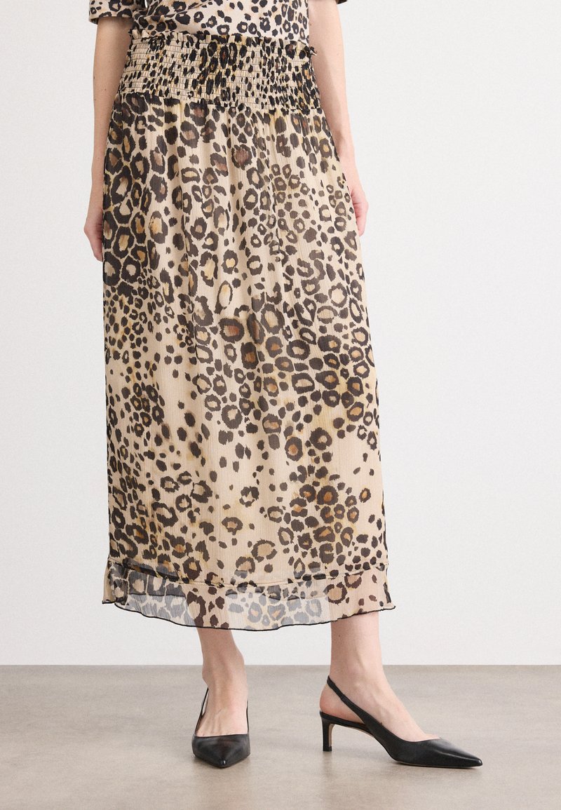 Jupe midi imprimée léopard en tissu transparent avec une taille smockée, offrant une forme évasée et un détail d'ourlet subtil, associée à des escarpins noirs.