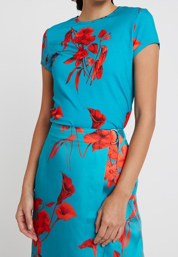 Conjunto turquesa que presenta una blusa ajustada y una falda a juego, ambas adornadas con vibrantes estampados florales rojos y una textura de tela suave y lisa.
