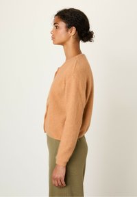 Kerge oranž, koheline kardigan ümmarguse kaelusega, pika varrukaga ja nööpide kinnitusega. Kombineeritud rohelise seelikuga kontrasti loomiseks.