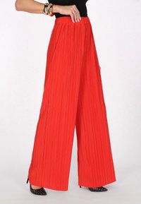 Red, pleated wide-leg pants with an elastic waistband. Features vertical stripes and a smooth texture, paired with black, pointed-toe heels.