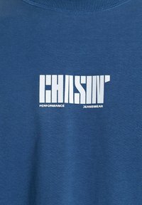 Kék pamut pulóver, amelynek élénk fehér grafikája a "CHASIN' PERFORMANCE JEANSWEAR" feliratot tartalmazza. Klasszikus, kerek nyakú dizájn.