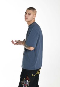 Graphic t-shirt in blue cotton with a round neckline and short sleeves, paired with black pants featuring a dragon embroidery detail.