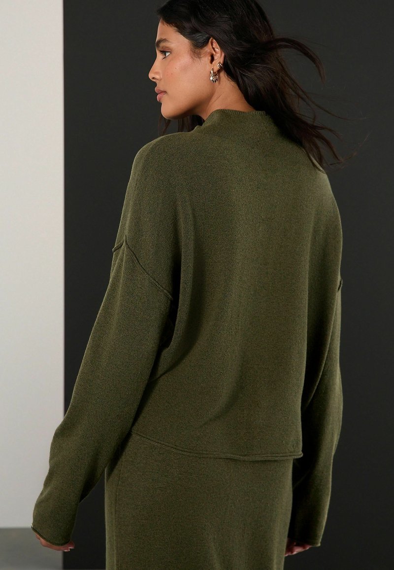 Oliwkowy, oversize sweter z okrągłym dekoltem, długim rękawem i teksturowanym materiałem. Ma opadające ramiona i luźny krój.