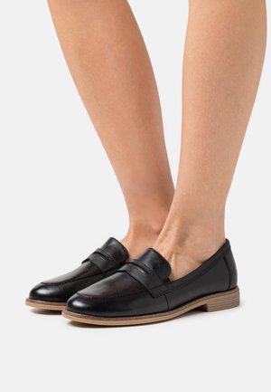 Schwarze Lederloafers mit glatter Oberfläche, runder Zehenform und einem dekorativen Riemen über dem Spann; flache, beige Sohle.