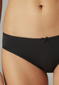 Black cotton briefs featuring a lace trim and a small bow detail at the waistband. Smooth texture with a classic cut design.