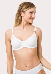 White bra featuring adjustable straps, smooth fabric, and a seamless design. Accented with a delicate trim along the edges.