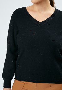 Schwarzer V-Ausschnitt-Pullover mit langen Ärmeln, der mit verstreuten funkelnden Akzenten, gestrickter Textur und gerippten Bündchen und Saum ausgestattet ist.